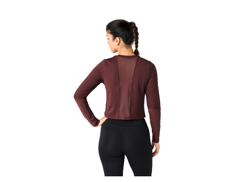 Une femme porte un haut bordeaux à manches longues et des leggings noirs.
