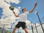 Man in wit T-shirt en zwarte korte broek speelt padel met racket en bal.