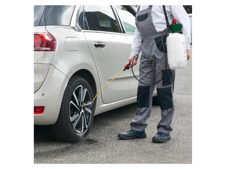 Man in overall reinigt autobanden met een drukspuit.