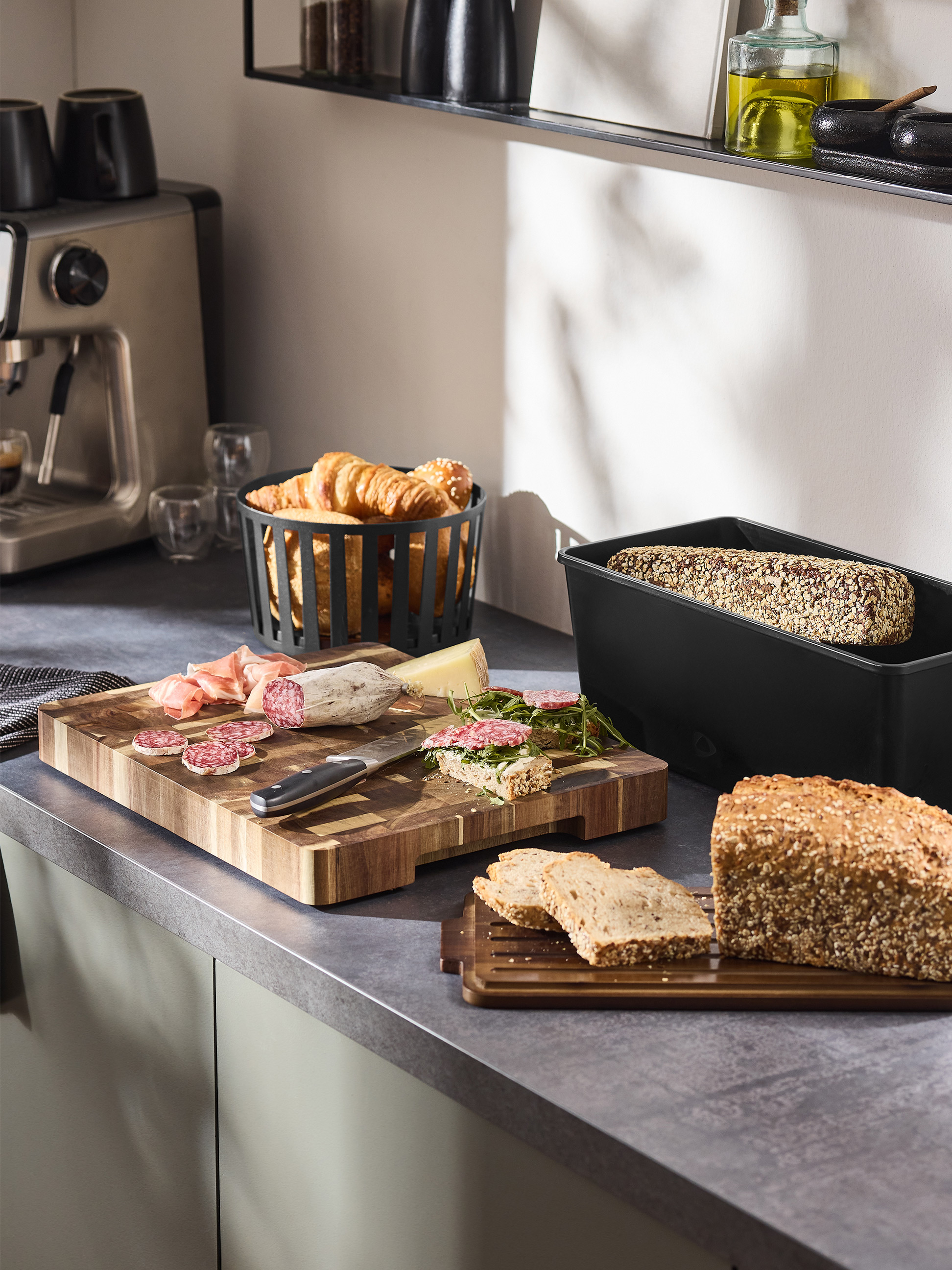 Petit-déjeuner avec machine à café, pain, charcuterie et croissants sur un comptoir de cuisine.
