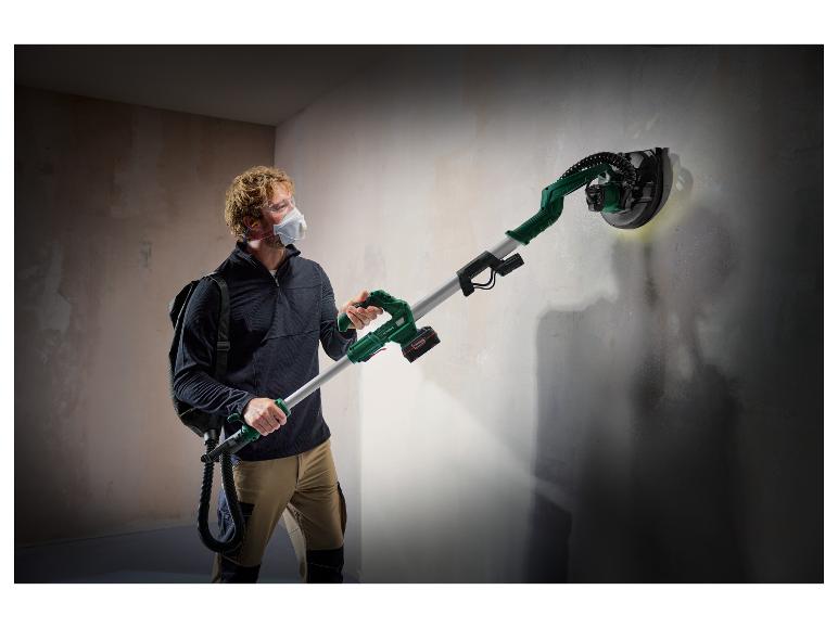 Een man schuur een muur met een lange, groene schuurmachine.