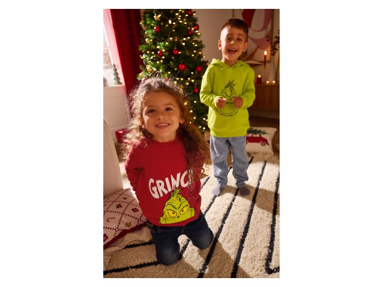 Deux enfants souriants portent des sweats à capuche sur le thème du Grinch près d'un sapin de Noël.