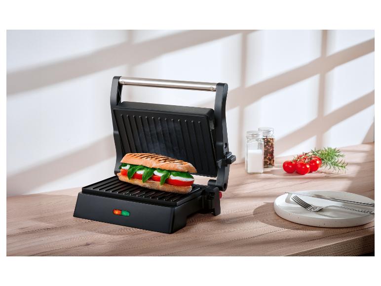 Open paninipers met een Caprese sandwich op een houten aanrecht.