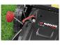 Gros plan d'une tondeuse à gazon avec une poignée rouge et des roues noires sur l'herbe verte.