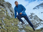 Un homme avec une veste en polaire bleue et un pantalon bleu foncé, marche sur une montagne rocheuse