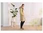 Vrouw in een lange beige puffer bodywarmer en gele gebreide trui, staand binnenshuis.
