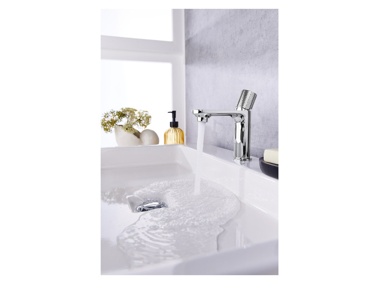 Een moderne wastafelkraan met een strak design, water dat in de wastafel stroomt.