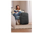 Une femme assise sur un canapé avec une valise et un guide de voyage.