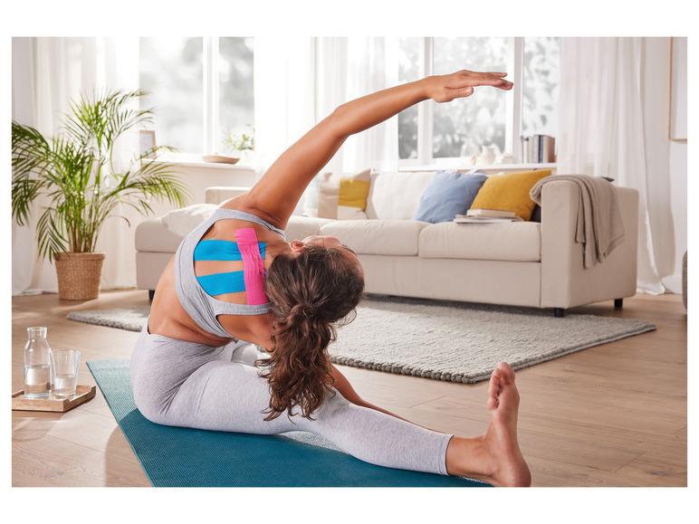 Femme faisant du yoga avec du kinésiotape sur un tapis bleu.