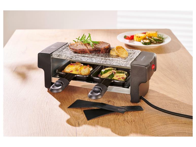 Appareil à raclette avec steak, pommes de terre et courgettes sur une table en bois.