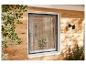Raam met hor aan houten wand, met planten en zonlicht.