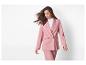 Vrouw in een roze pak met blazer en broek, met wapperend haar