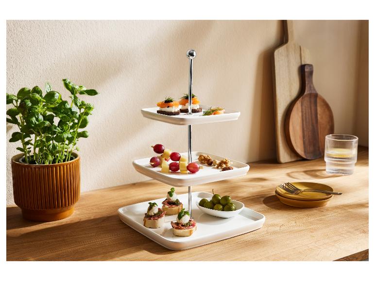 Un présentoir à trois niveaux avec des amuse-gueules variés, à côté d'un pot de basilic et d'ustensiles de cuisine.