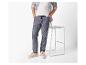 Man in blauwe broek met trekkoord, wit T-shirt en gestreept overhemd, naast een barkruk.