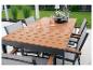 Buiten eethoek met houten tafel en grijze stoelen op een terras, met groen op de achtergrond.