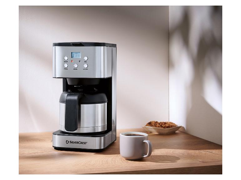 Cafetière SilverCrest en acier inoxydable avec tasse de café et biscuits sur un comptoir en bois.