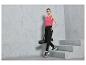 Een vrouw in een roze tanktop en zwarte joggingbroek met Let's Sport-logo, draagt een yogamat.