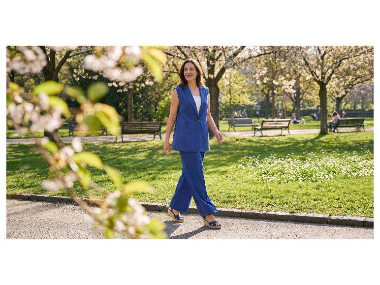 Femme en costume bleu avec gilet et pantalon large marchant dans un parc.