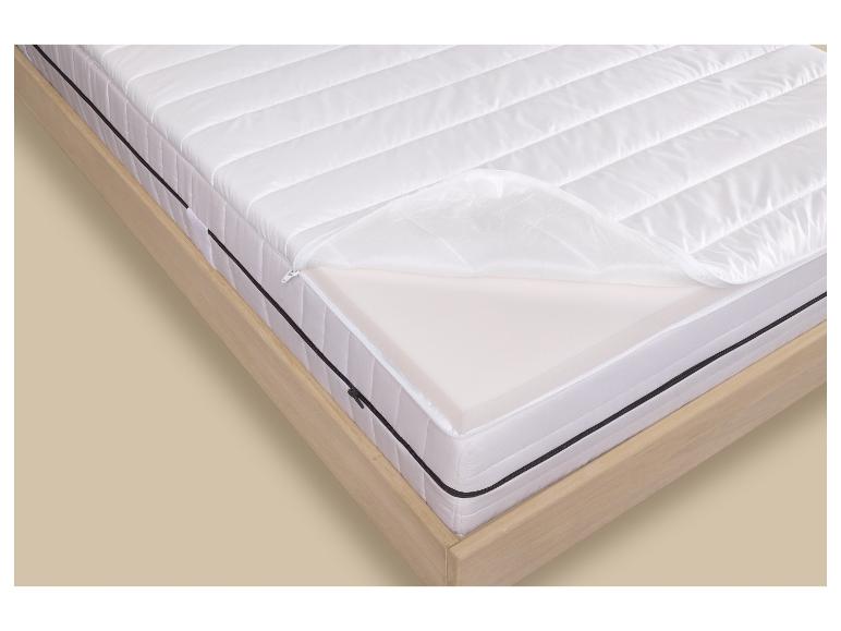 Wit matras met open rits die de binnenste schuimlaag toont, op een houten bedframe.