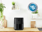 Zwarte airfryer op een houten aanrecht met planten en planken.