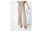 Vrouw in een beige getextureerde top met korte mouwen en wijde broek, met bruine sandalen.