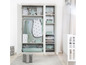 Une chambre de bébé avec une armoire blanche pleine de vêtements pour bébé, un sac de couchage et un lit bébé.