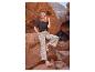 Femme en t-shirt noir et pantalon à motifs floraux assise sur un rocher dans un canyon.