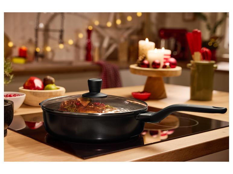 Poêle noire avec couvercle en verre sur une plaque de cuisson, avec décor festif en arrière-plan.