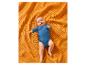 Een schattige baby in een blauwe romper liggend op een oranje getextureerde deken.