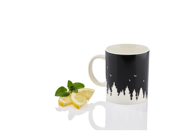 Une tasse noire avec un imprimé de forêt, des tranches de citron et des feuilles de menthe.