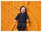 Lachende baby in zwarte hoodie, liggend op een oranje deken.