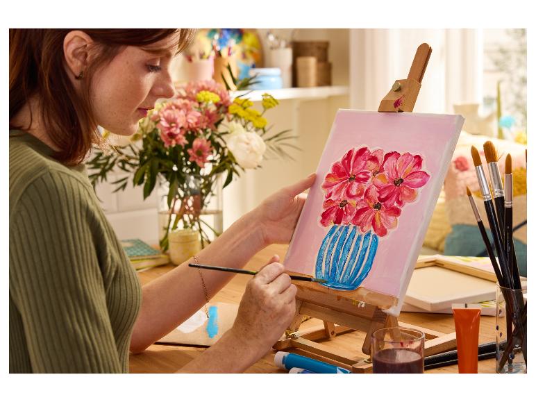 Une femme peint à l'acrylique un tableau de fleurs dans un vase.
