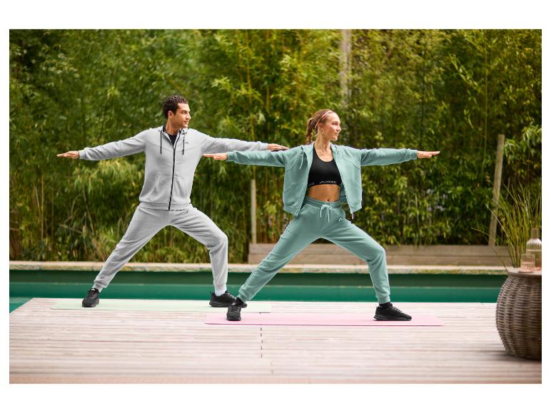 Deux personnes en survêtements et chaussures de sport faisant du yoga en extérieur sur une terrasse en bois.