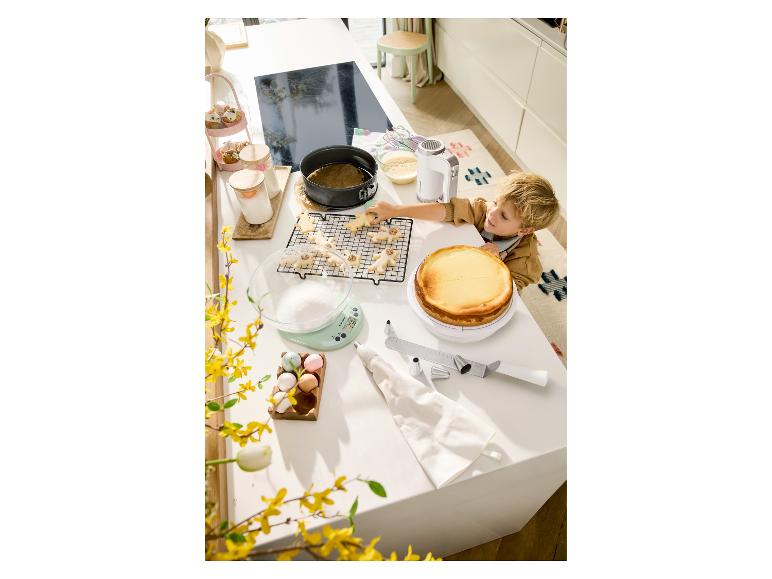 Garçon décorant des biscuits de Noël sur un comptoir de cuisine avec un gâteau et des fournitures de pâtisserie.