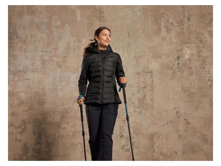 Een vrouw in een zwarte winterjas en wandelstokken.