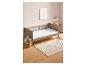 Een babybed met een wit dekbed en een vloerkleed met stippen.