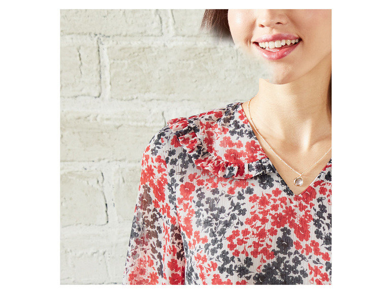 Een vrouw draagt een roze blouse met bloemenprint en een zilveren ketting.