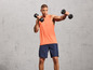 Man in een oranje tanktop met zwarte dumbbells tijdens het trainen.