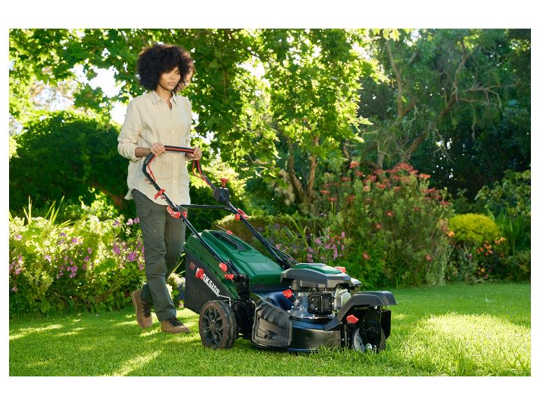 Une femme utilise une tondeuse à gazon Parkside dans un jardin fleuri.