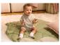 Lachende baby zit op een groene mat, met een houten rammelaar.
