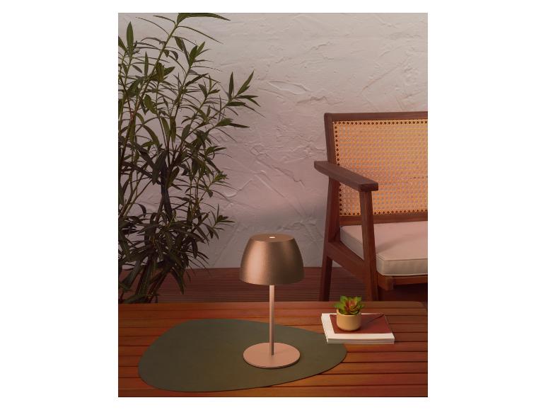 Lampe de table portable sur une table en bois, avec des plantes et une chaise en arrière-plan.