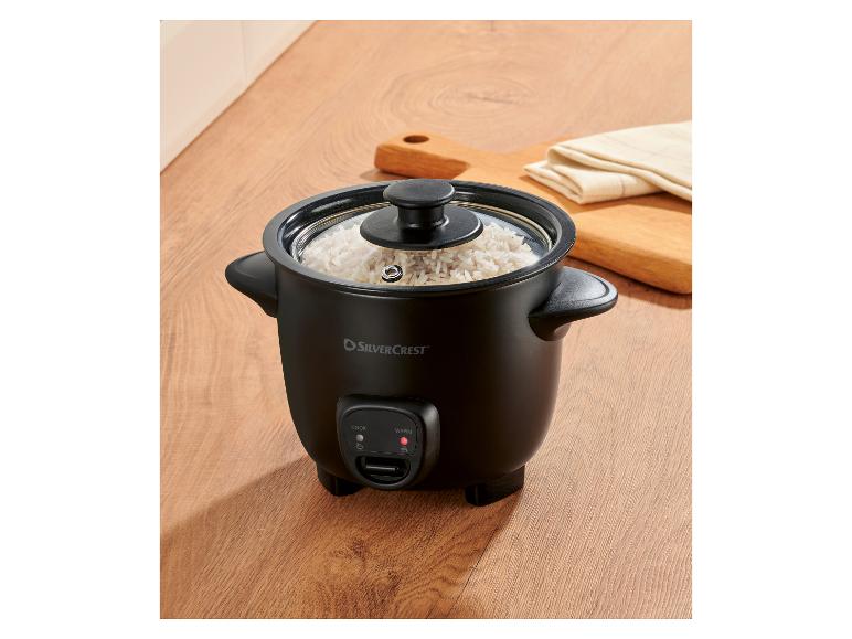 Zwarte rijstkoker met glazen deksel, gevuld met gekookte rijst, op een houten ondergrond.
