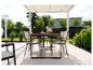 Tuineetset met tafel en stoelen onder een pergola, omringd door groen.