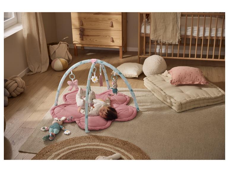 Baby op roze speelmat met speelboog, omringd door kinderkamerdecoratie.