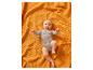 Blije baby in een grijze romper liggend op een oranje wafeldekentje.