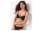 Femme souriante en soutien-gorge et culotte noirs, appuyée contre un mur blanc