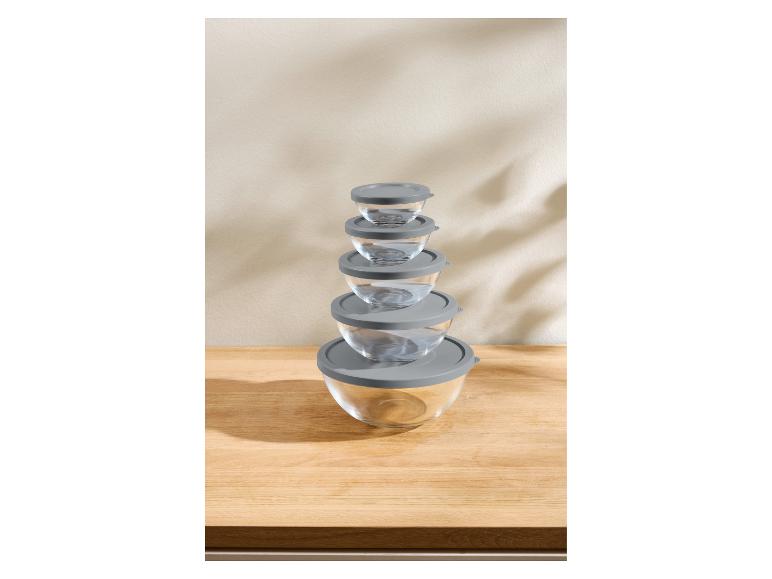 Ensemble de cinq bols en verre avec couvercles gris, empilés sur un comptoir en bois.