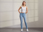 Een vrouw draagt ​​een witte tanktop en blauwe skinny jeans.