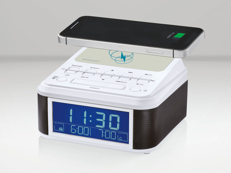 Un réveil radio Silvercrest blanc avec un écran numérique et un haut-parleur intégré, sur lequel se trouve un smartphone.