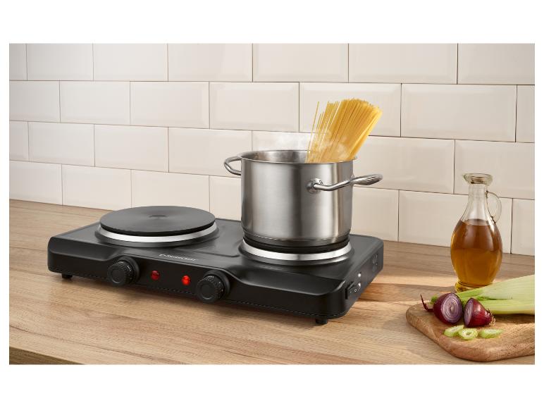 Plaque de cuisson électrique portable avec une casserole de spaghettis bouillants, de l'huile et des légumes coupés.